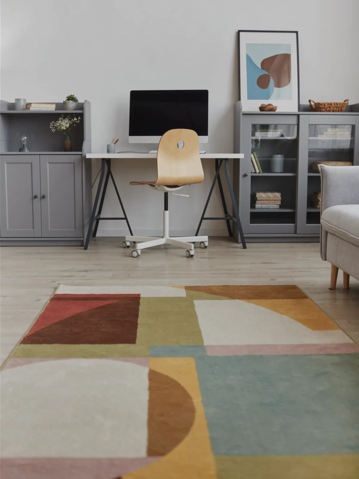A modern home office featuring a stylish geometric rug, a minimalist desk setup with a computer, and sleek gray storage cabinets, creating a productive and inviting workspace.
