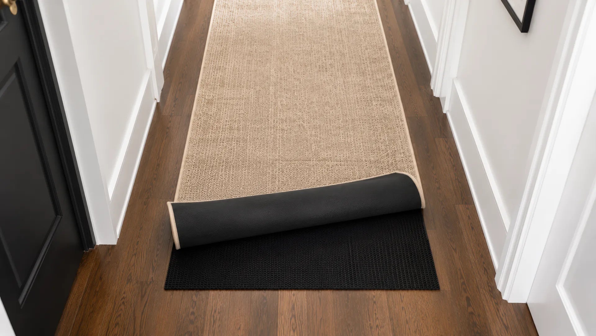 A beige rug unrolled on a rug pad in a hallway. A black door and white walls.
