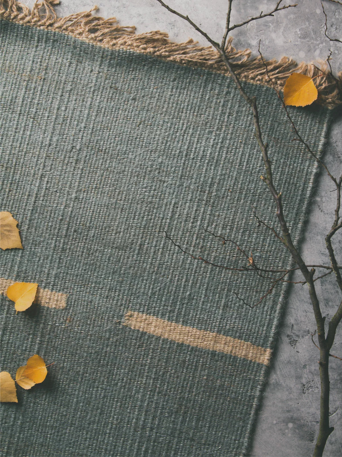 Close-up of an 8x10 jute rug with a woven texture and fringed edges, set against a rustic concrete floor with autumn leaves scattered around.