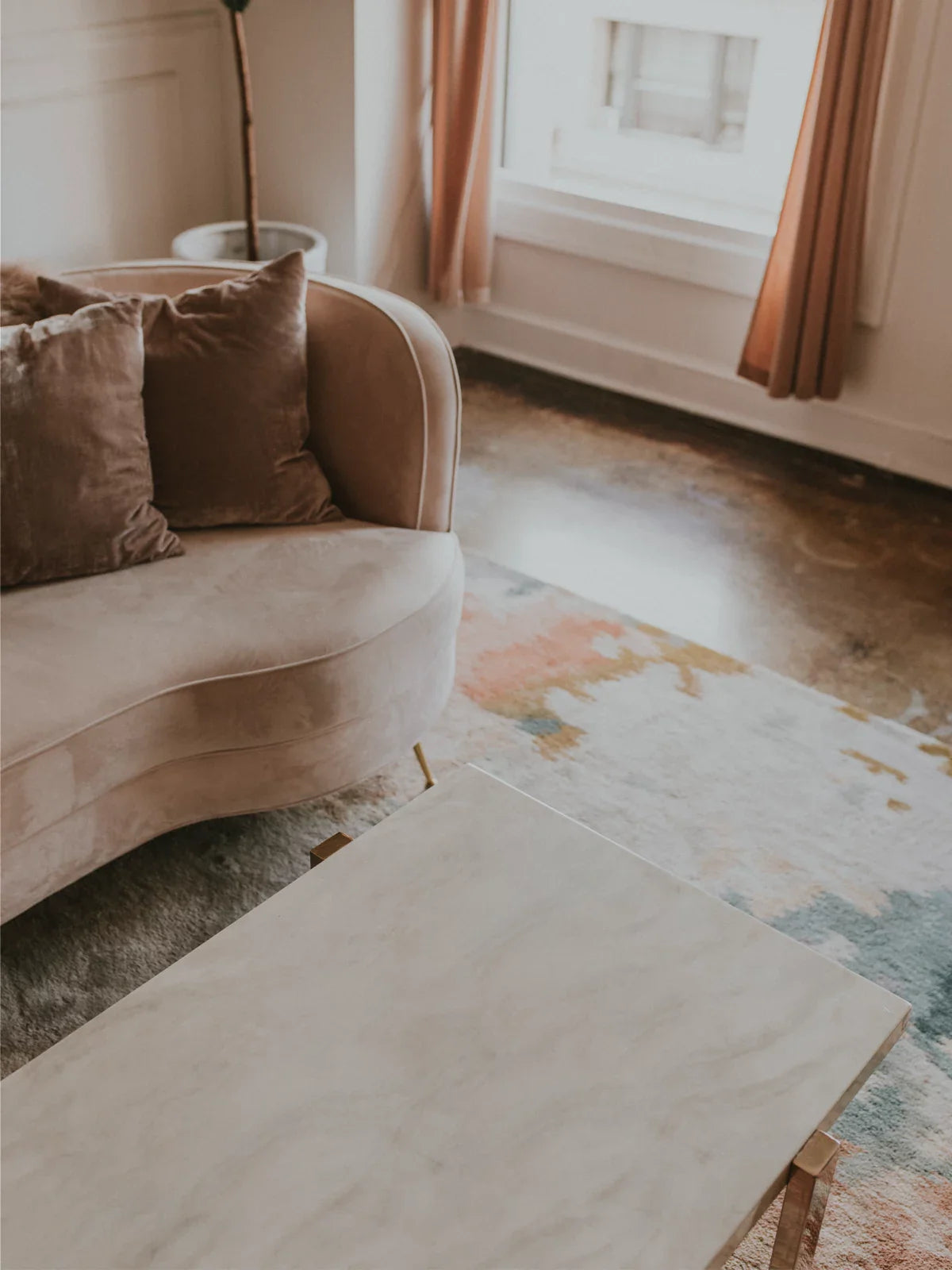  luxurious wool rug with a soft, artistic pattern, placed under a cozy velvet sofa in a stylish living room.