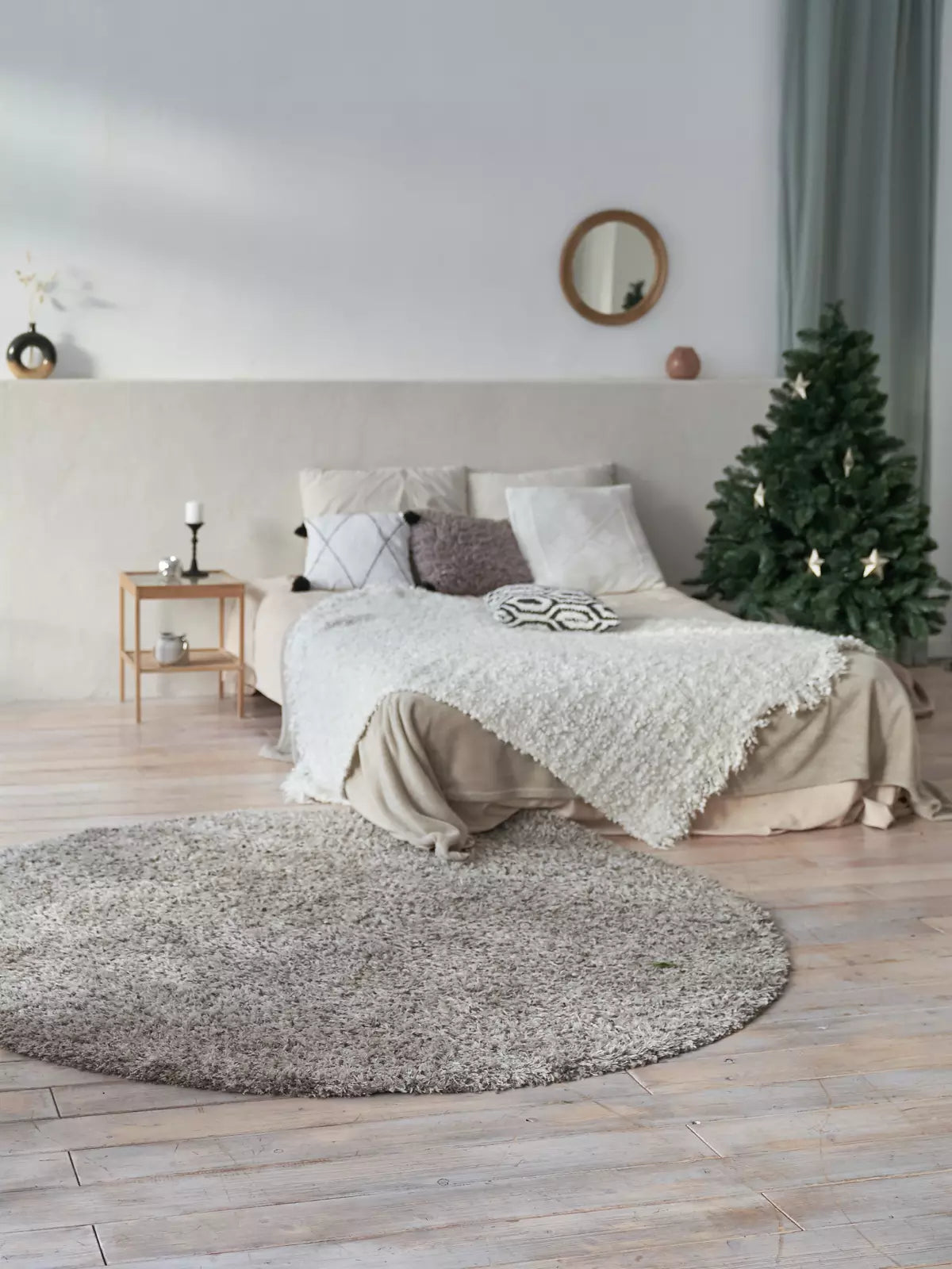 Cozy bedroom with a neutral-toned round washable rug on a light wooden floor, complementing a soft, textured bedspread and minimalist decor.