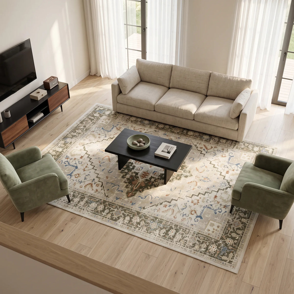 A styled living room scene showing a large patterned area rug on a light wood floor, with a beige sofa, two green armchairs, a black coffee table, and a TV in the background.