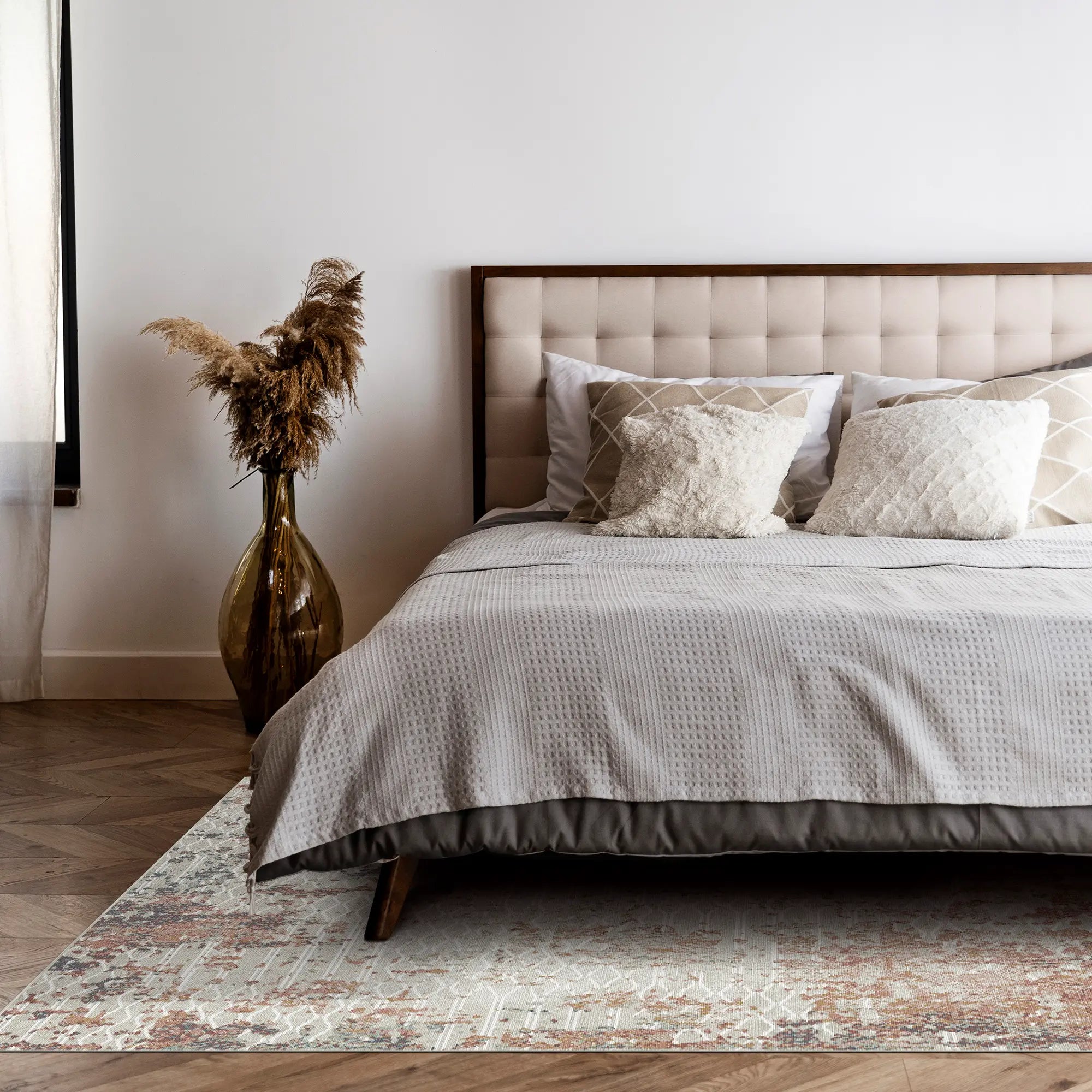 area rug with rust, beige, and gray abstract lattice pattern under bed on wood floor