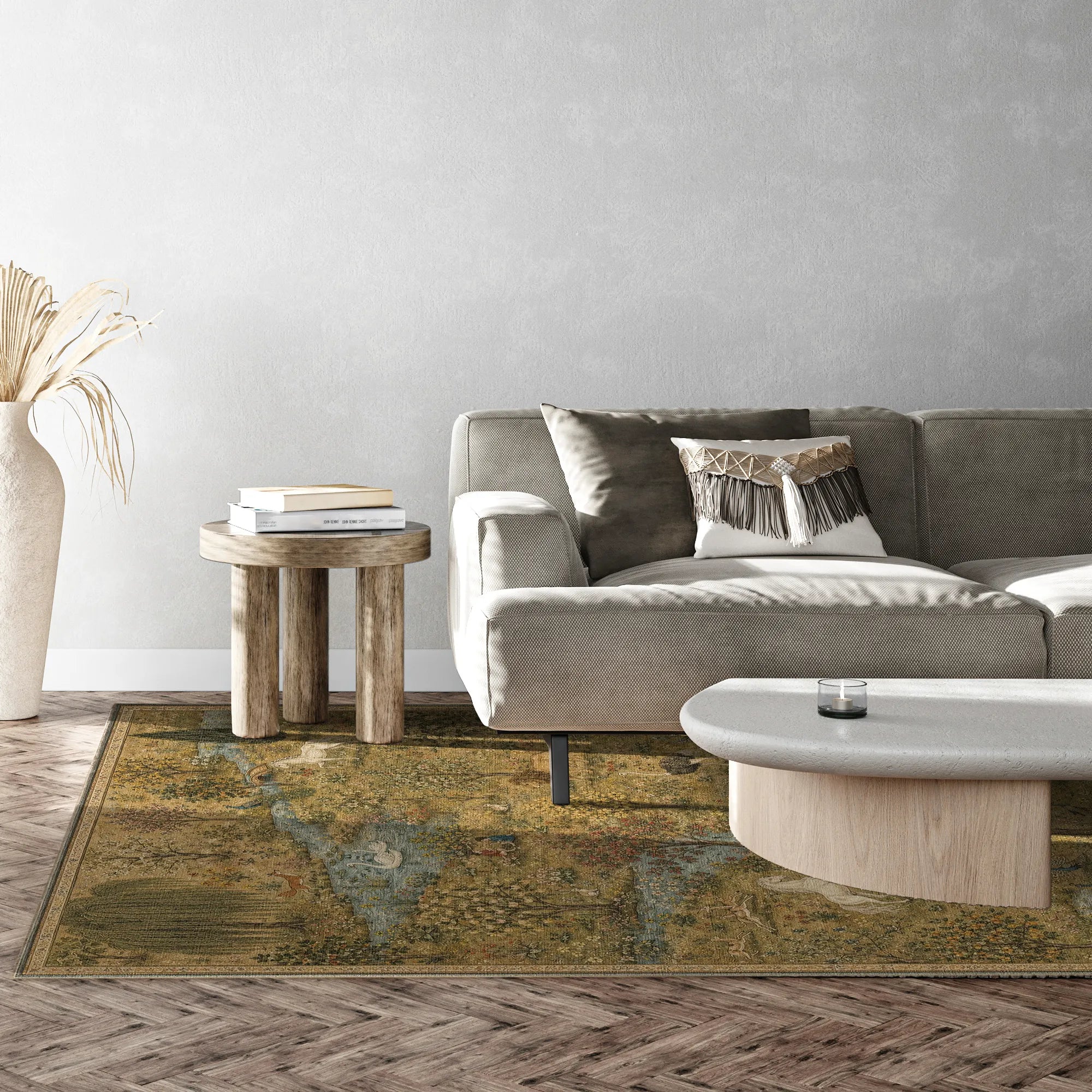 A rectangular area rug with an abstract, distressed paint-splatter pattern in olive green, brown, and beige tones, styled in a living room setting under a gray sofa and a light wood coffee table.