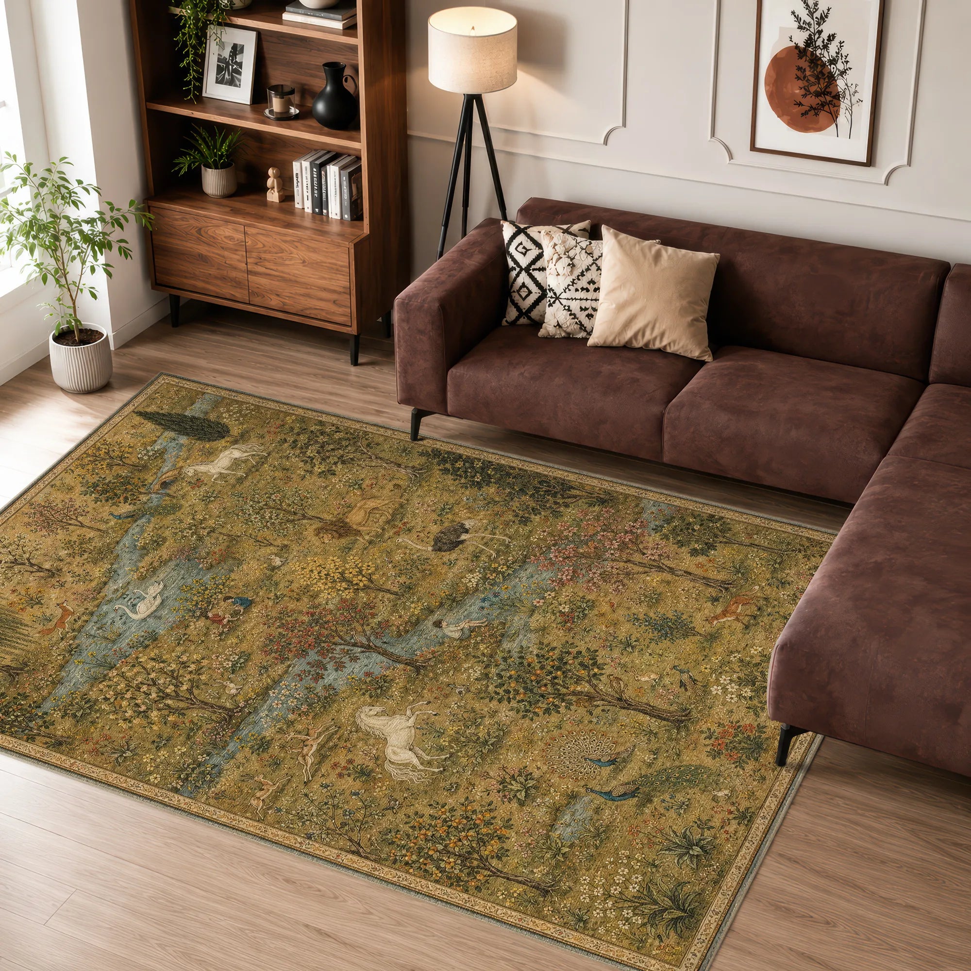 A rectangular area rug with an intricate, vintage-style landscape print in muted gold, olive green, and blue tones, styled in a modern living room setting next to a brown sectional sofa.